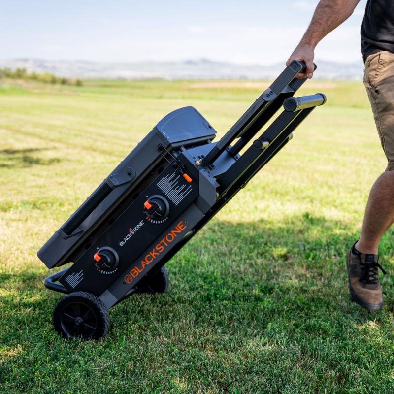 Person wheeling a folded Blackstone Omnivore griddle across a field